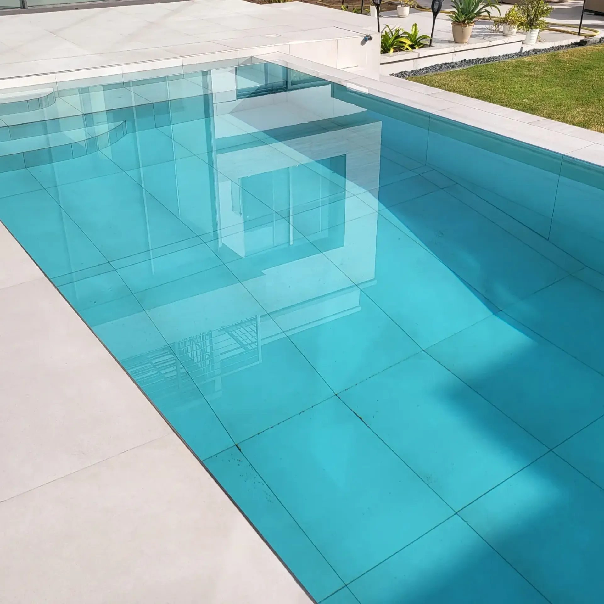 A turquoise pool with a glass side wall beside a modern villa