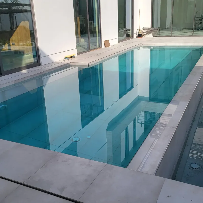 A turquoise pool with a glass side wall beside a modern villa
