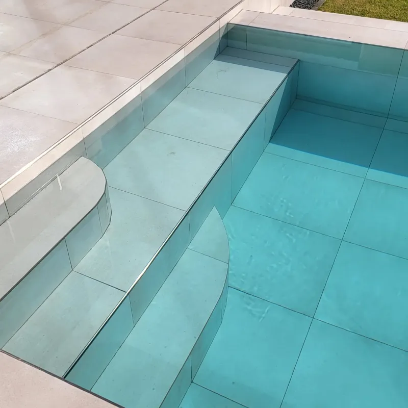 A turquoise pool with a glass side wall beside a modern villa