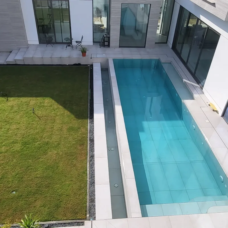 A turquoise pool with a glass side wall beside a modern villa