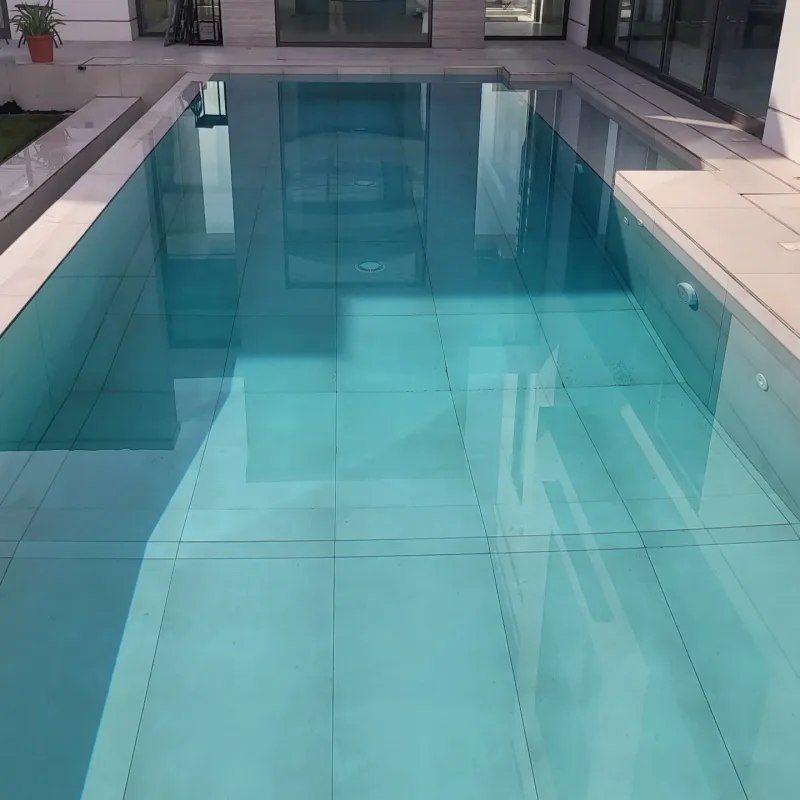 A turquoise pool with a glass side wall beside a modern villa