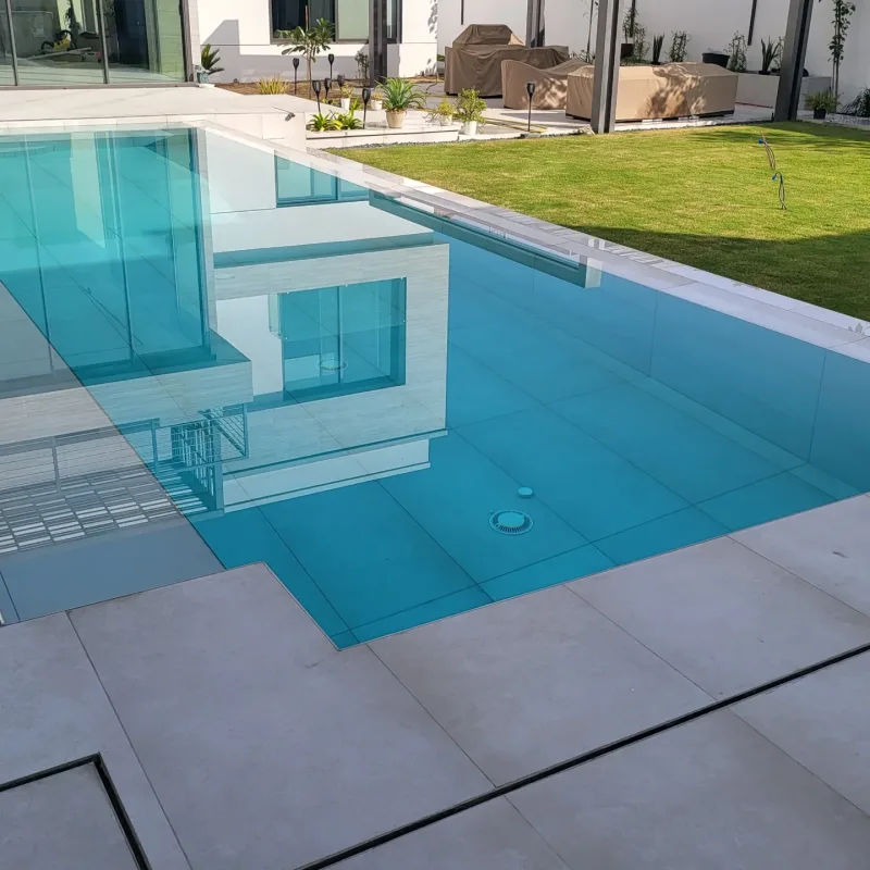 A turquoise pool with a glass side wall beside a modern villa