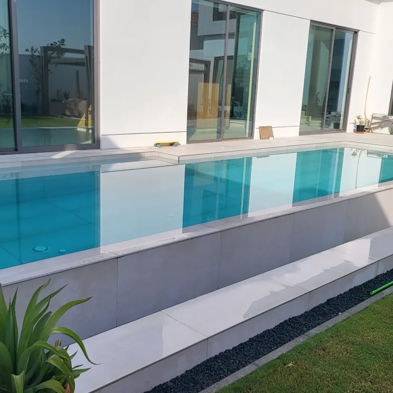 A turquoise pool with a glass side wall beside a modern villa