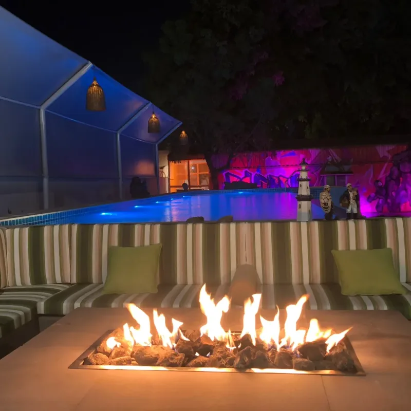 A villa pool beside a sunken seating terrace with a lit gas fire table