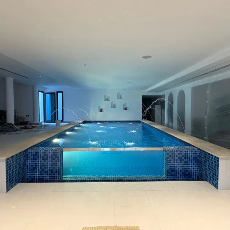 An indoor pool tiled in blue mosaic with lighting set into the ceiling
